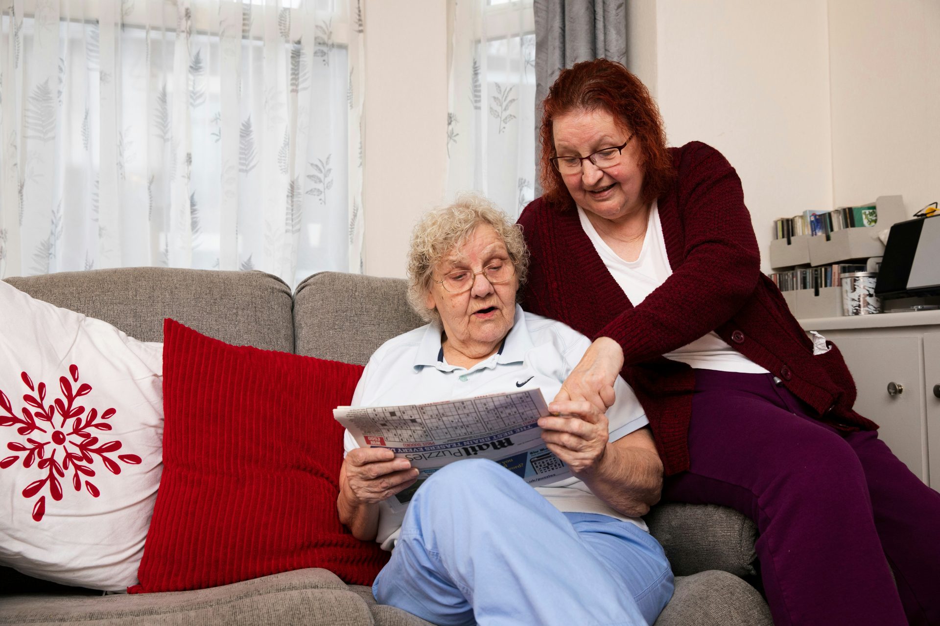 Two older ladies sat on the sofa looking at a newspaper